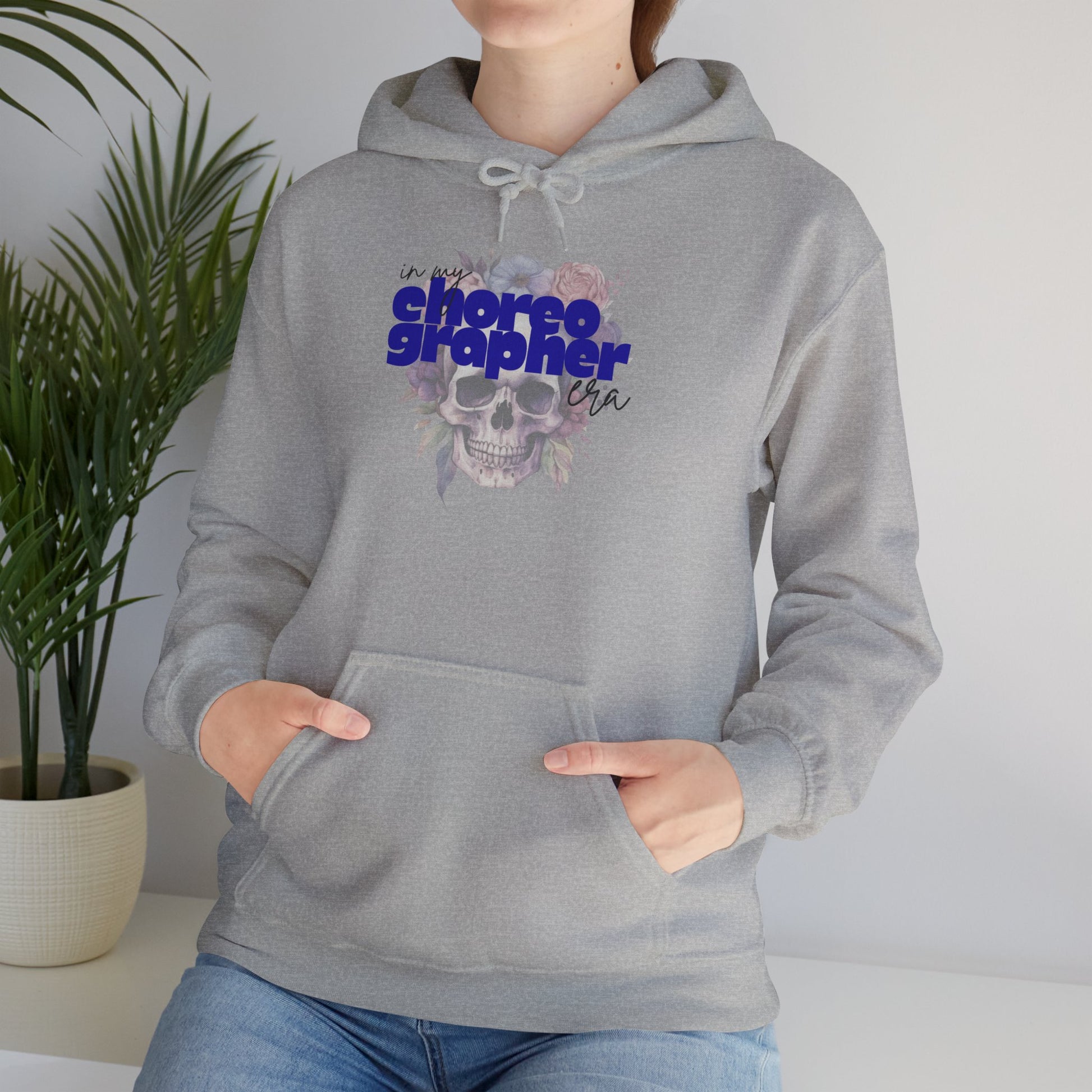 Person wearing a gray hoodie with a graphic design and text, standing against a neutral background.