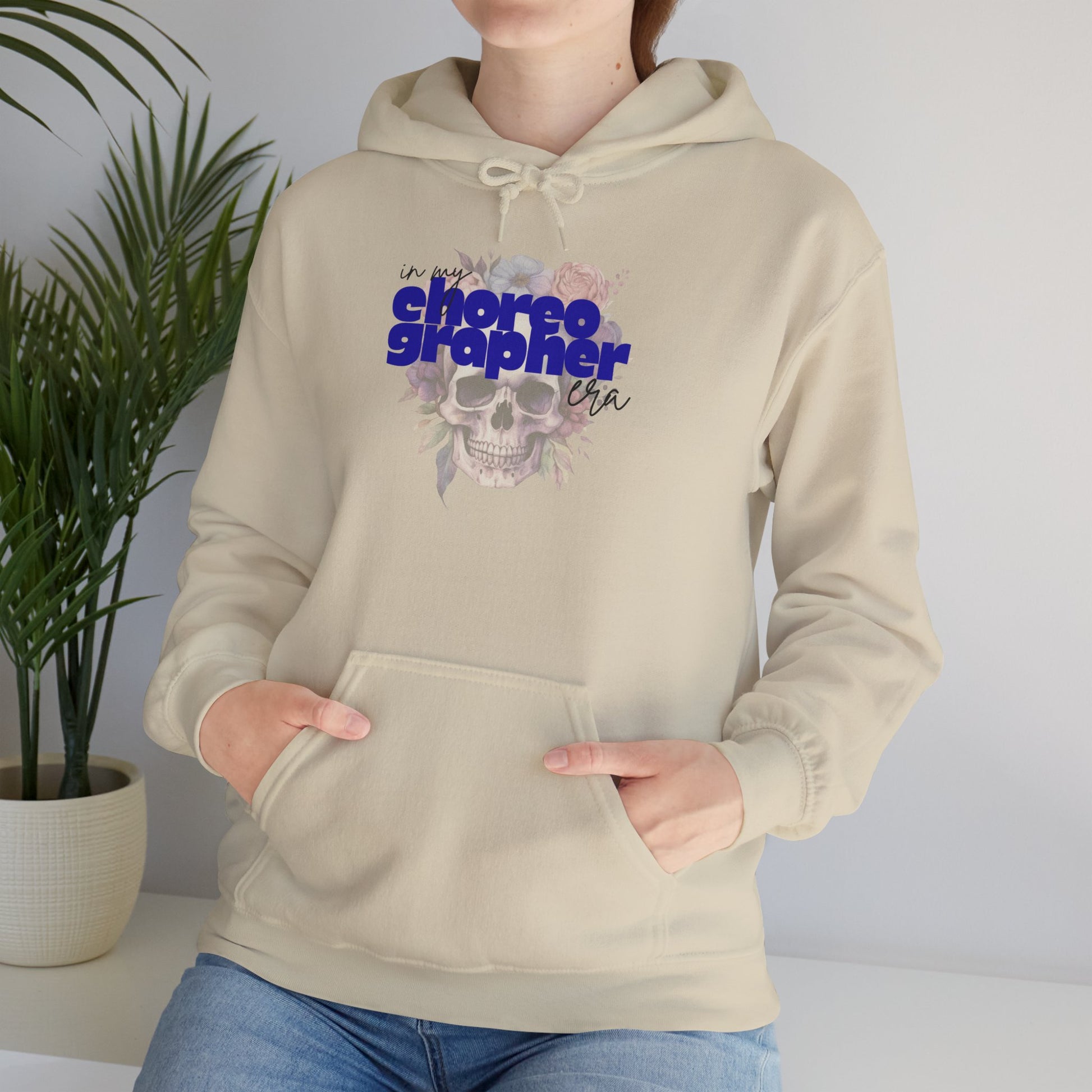 Person wearing a beige hoodie with a graphic design and text, standing against a plain background.
