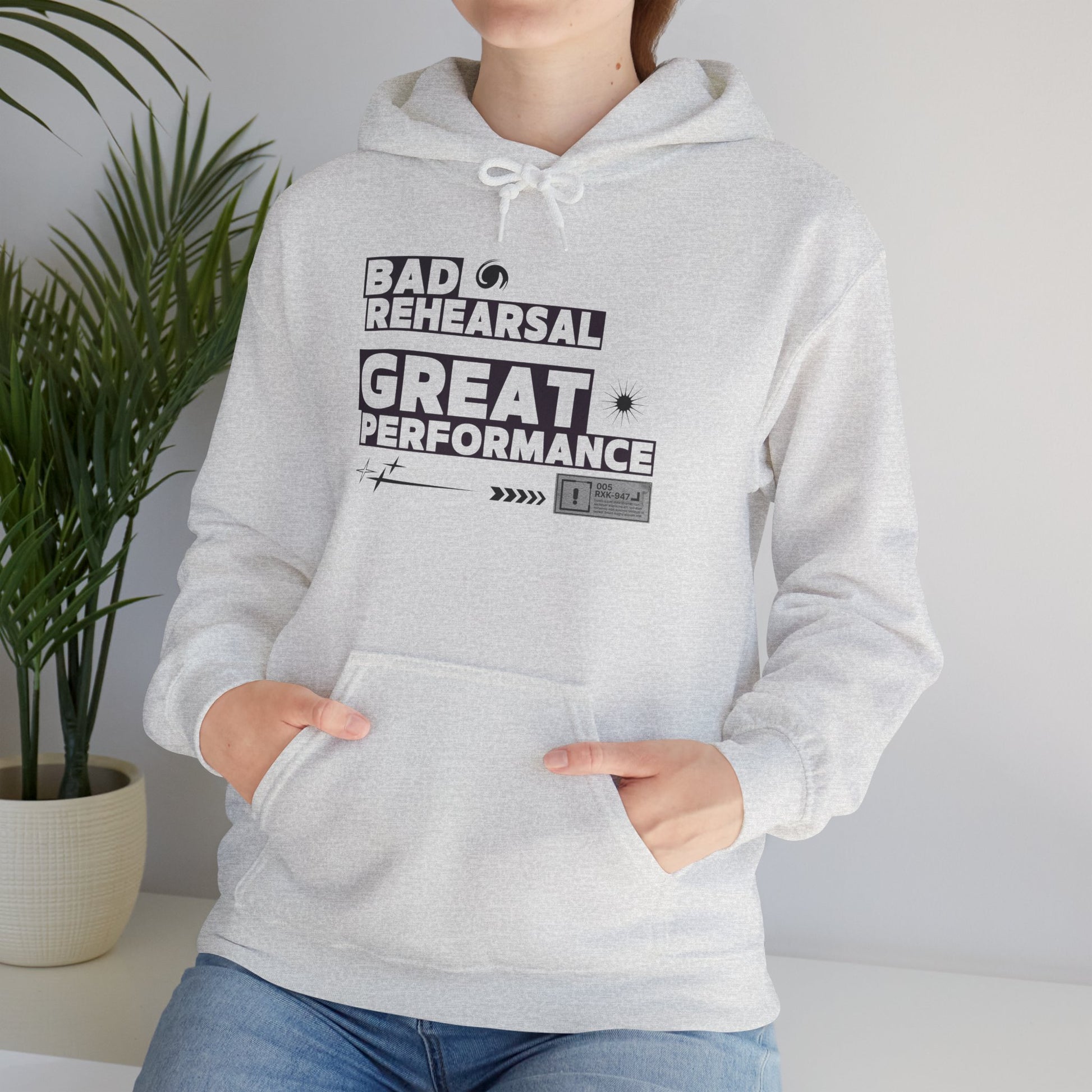 Person wearing a gray hoodie with text 'Bad Rehearsal Great Performance' in a minimal indoor setting.