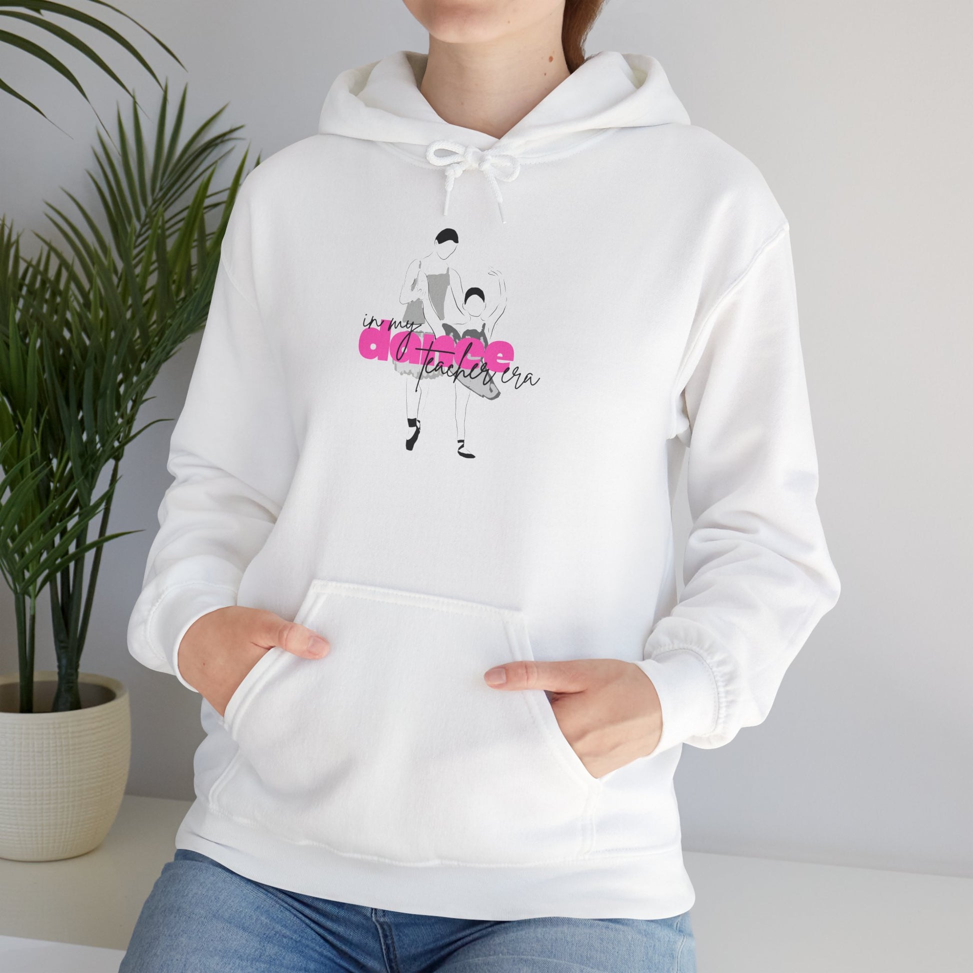 White hoodie with graphic design worn by a person, against a neutral background with a plant.