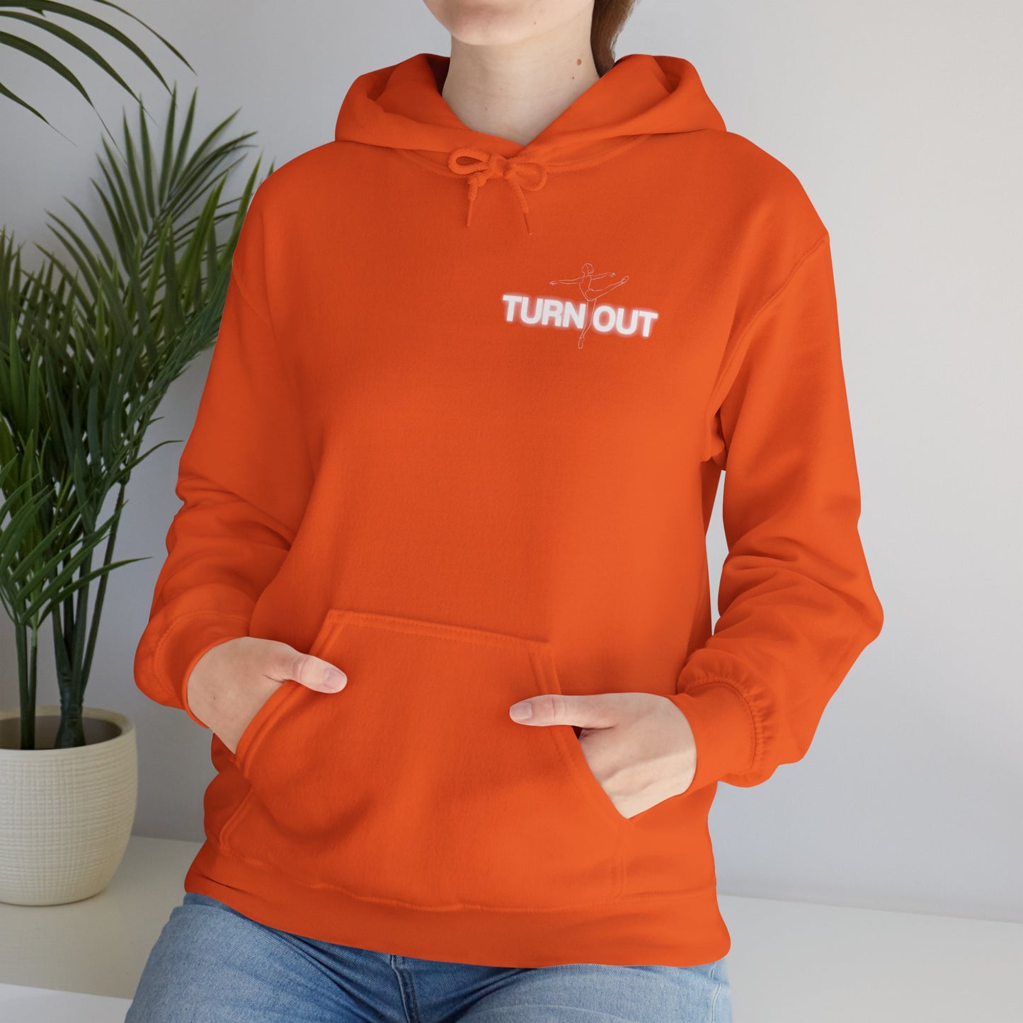 Person wearing an orange hoodie with 'TURN OUT' text, standing indoors with a plant in the background.