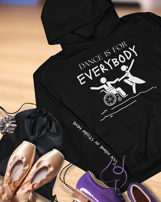 Black hoodie with 'Dance is for Everybody' text and wheelchair icon, placed on a wooden floor with ballet shoes.