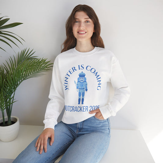 Person wearing a white sweatshirt with a blue graphic and text, sitting on a white surface with a plant in the background.