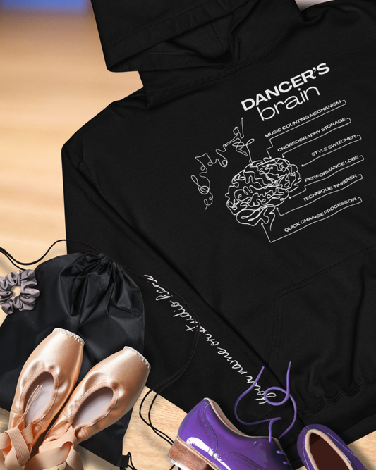 Black hoodie with 'Dancer's Brain' graphic and ballet shoes on a wooden floor.