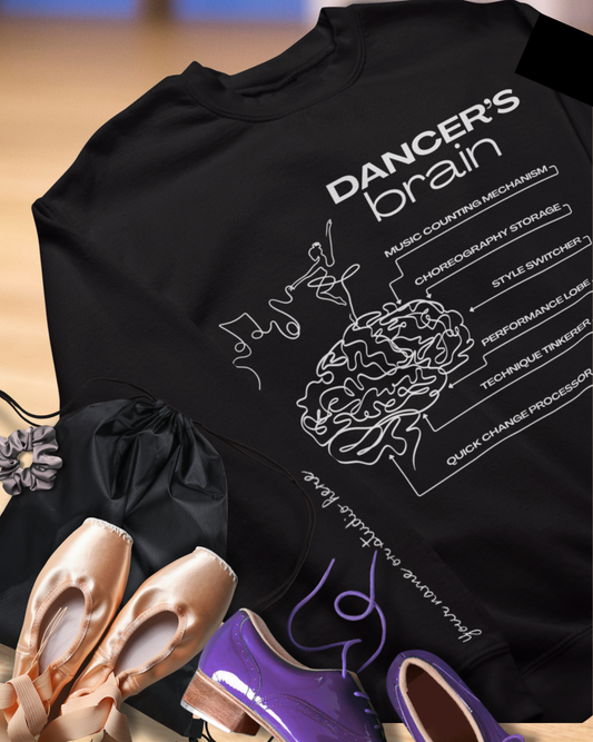 Black hoodie with 'Dancer's Brain' graphic and ballet shoes on a wooden floor.