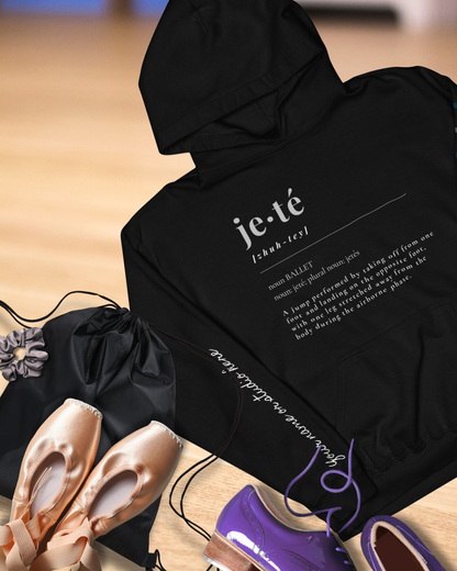 Black hoodie with text on a wooden floor with ballet shoes and a drawstring bag.